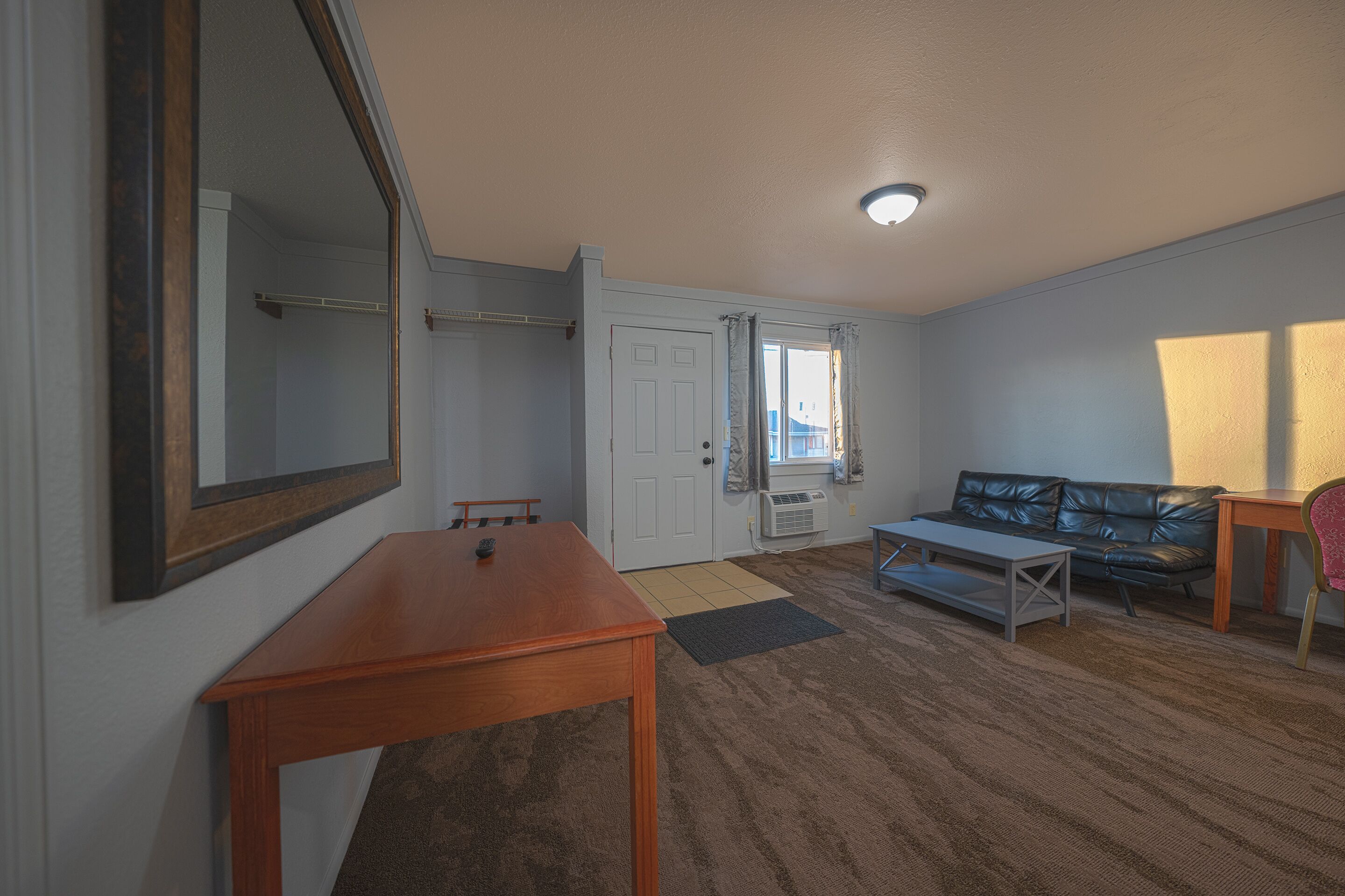 Una habitación con una mesa de madera, un sofá, un espejo y una puerta que da a otra estancia.