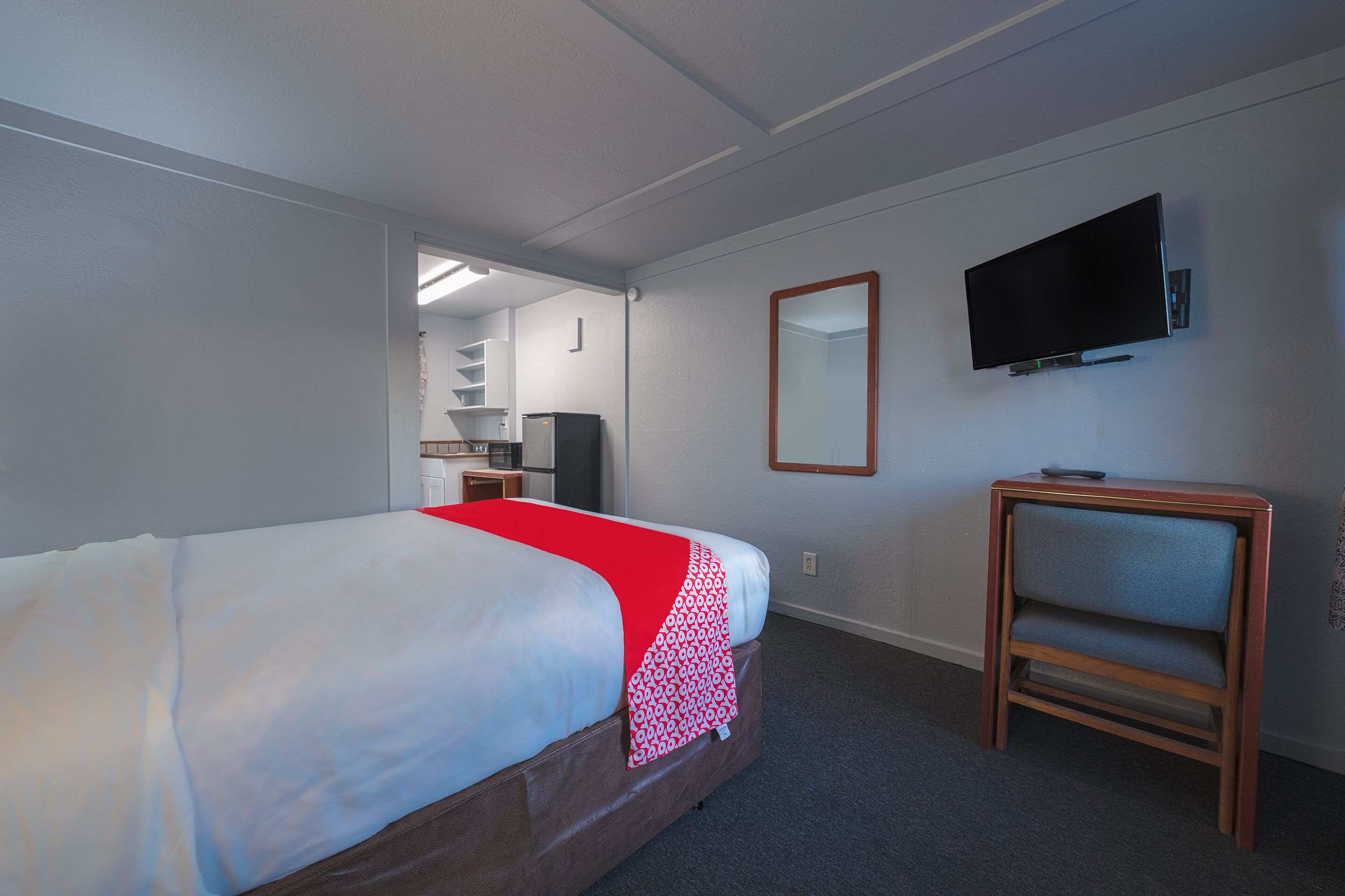 A hotel room with a bed, a TV mounted on the wall, a small wooden side table, and a mirror.