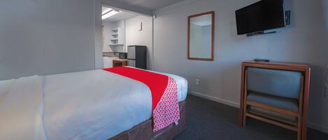 A hotel room with a bed, a TV mounted on the wall, a small wooden side table, and a mirror.