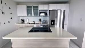 A modern kitchen with white cabinets, a stainless steel refrigerator, a microwave, and a black induction cooktop. - Ocean view apartment- close to beaches and Yunque (Luquillo)