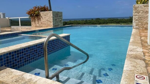 A swimming pool with a clear blue water, a metal ladder, and a view of the ocean. - Ocean view apartment- close to beaches and Yunque (Luquillo)