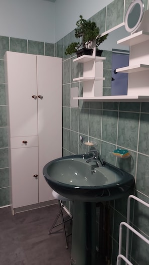 Ett badrum med ett grönt handfat, vita skåp och en krukväxt på en hylla.