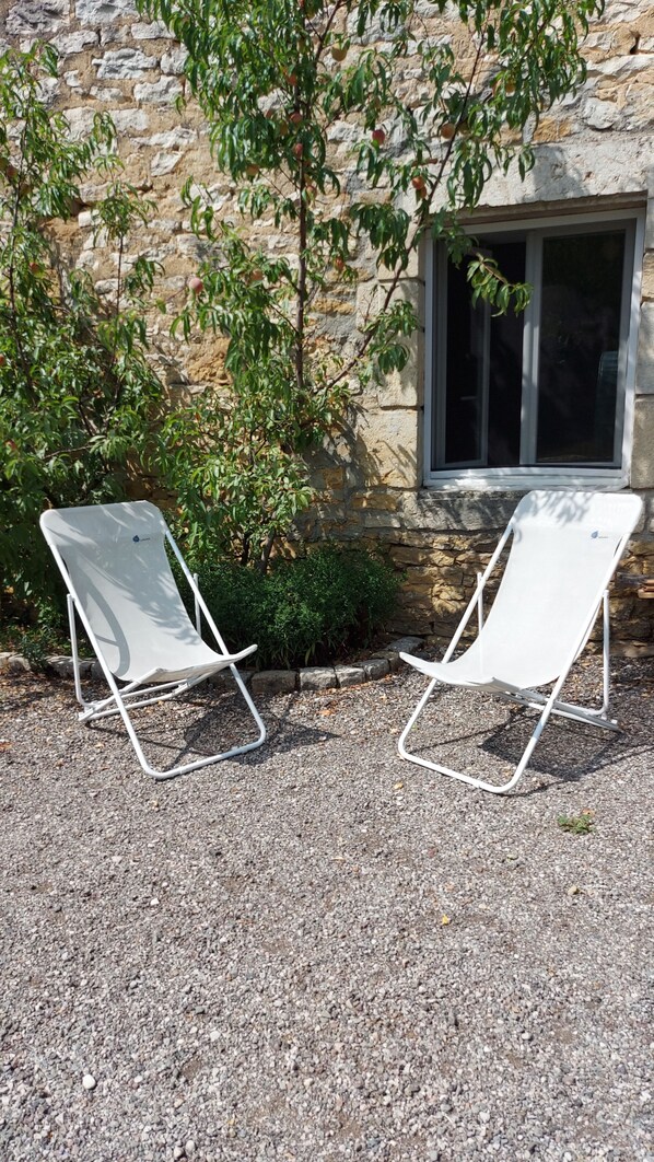 Two white lounge chairs outside a stone building with a window.
