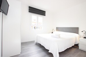 A modern bedroom with a large bed, bedside tables, a flat-screen TV, and a window with blinds. - RIERES. Modern apartment near the beach. (Puerto Pollensa)