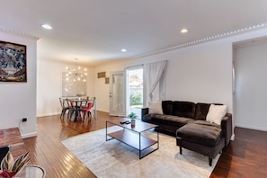 Ein modernes Wohnzimmer mit einem dunkelbraunen Sofa, einem Glastisch und einem Essbereich mit rundem Tisch und Stühlen.