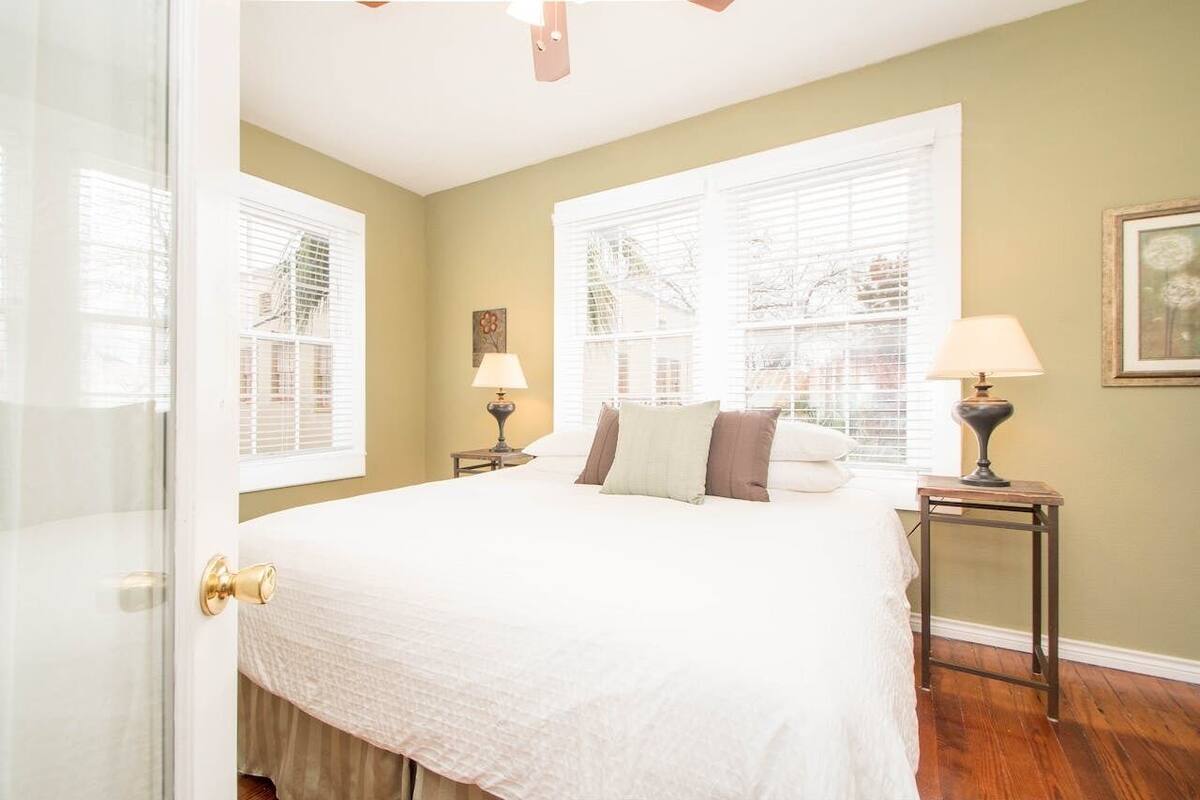Une chambre à coucher avec un grand lit, deux tables de chevet avec des lampes et une fenêtre avec des stores.