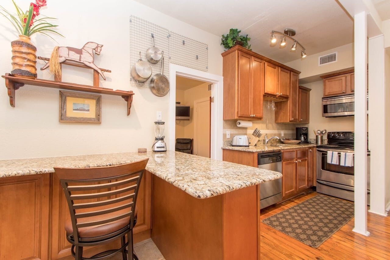 A kitchen with wooden cabinets, granite countertops, a built-in oven, and a hanging pot rack.