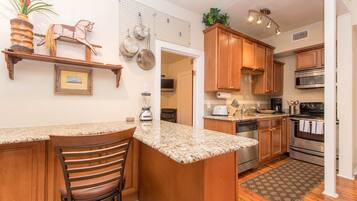 A kitchen with wooden cabinets, granite countertops, a built-in oven, and a hanging pot rack.