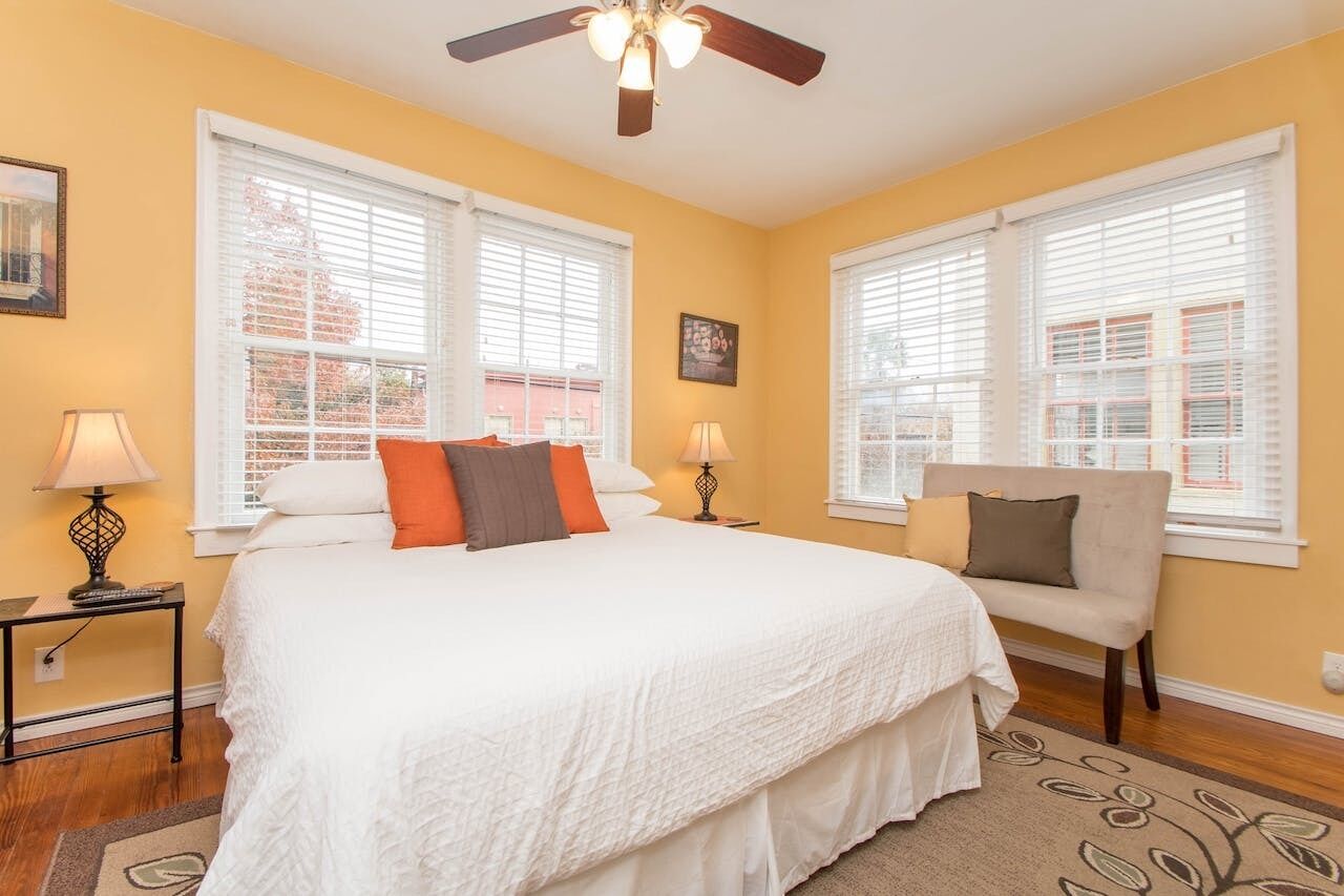 A bedroom with a large bed, two bedside tables with lamps, a chair, and a ceiling fan.