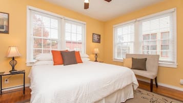 A bedroom with a large bed, two bedside tables with lamps, a chair, and a ceiling fan.