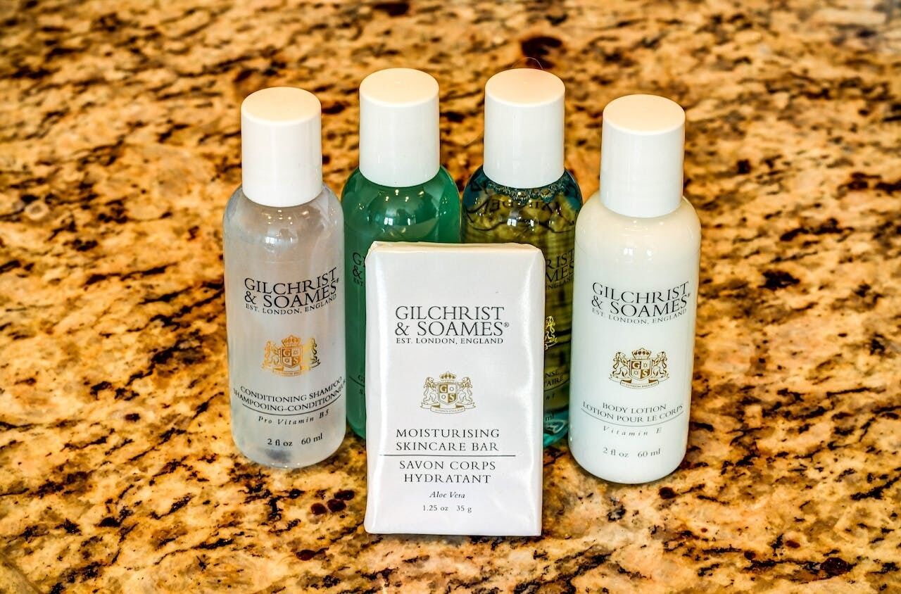 Quatre flacons de produits de soins pour la peau de la marque Gilchrist & Soames et un savon sur un comptoir en granit.