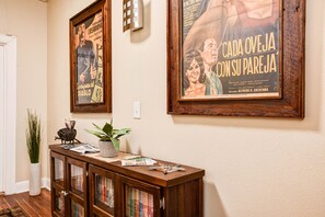 A hallway with a wooden console table displaying books and decorative items, flanked by two framed movie posters on the wall. - The Madison Riverwalk (San Antonio)