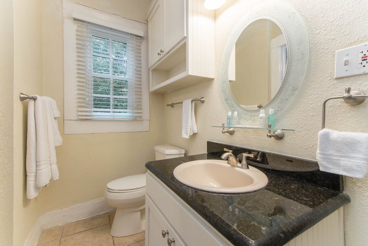 A bathroom with a toilet, sink, mirror, and window.