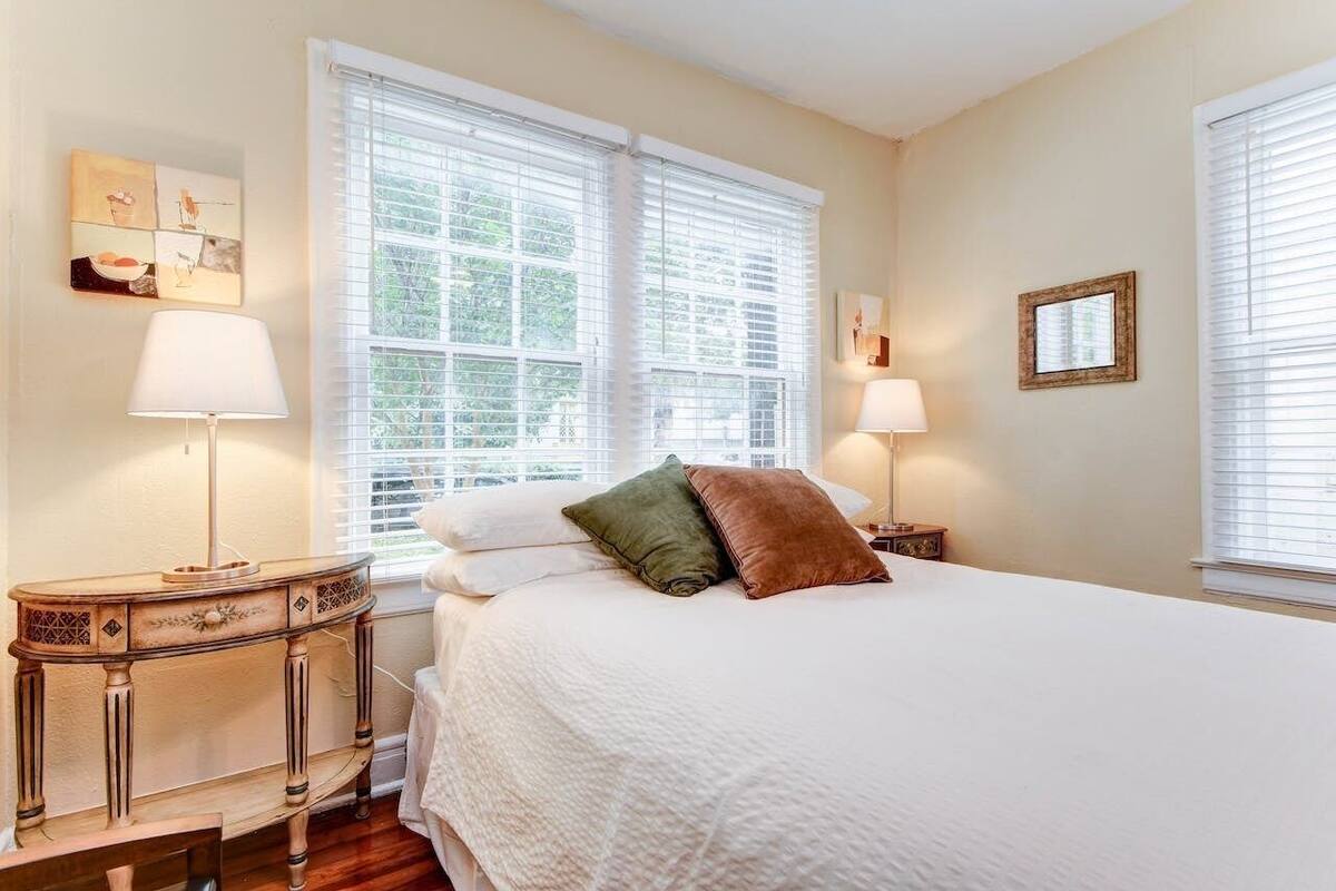 Une chambre à coucher avec un grand lit, deux tables de chevet avec des lampes et une fenêtre avec des stores.