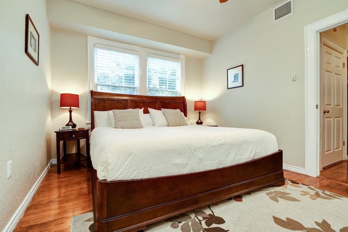 Une chambre à coucher avec un grand lit, deux tables de chevet avec des lampes, une fenêtre avec des stores et une porte.
