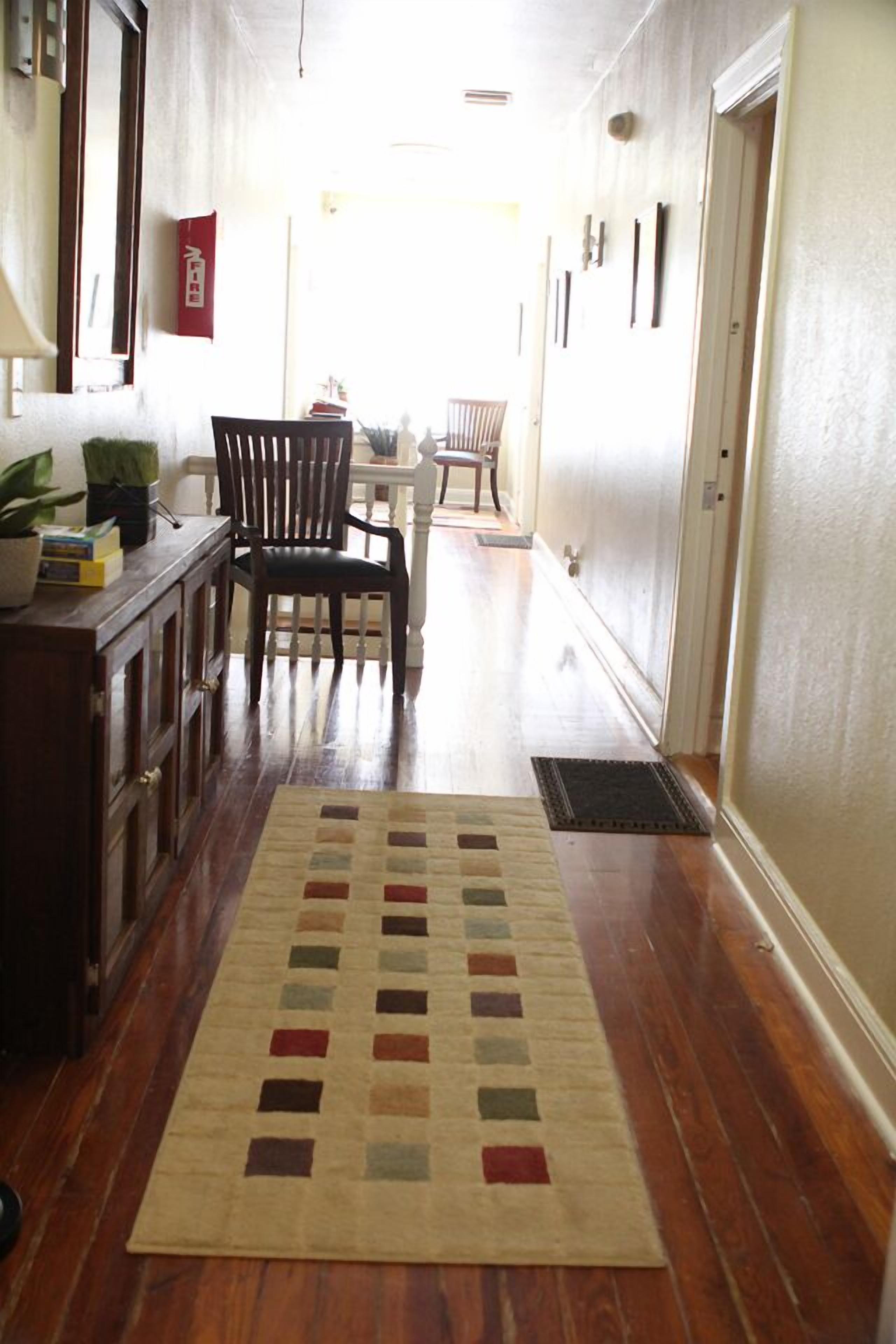 A hallway with a wooden floor, a rug, a dining table with chairs, and a cabinet.