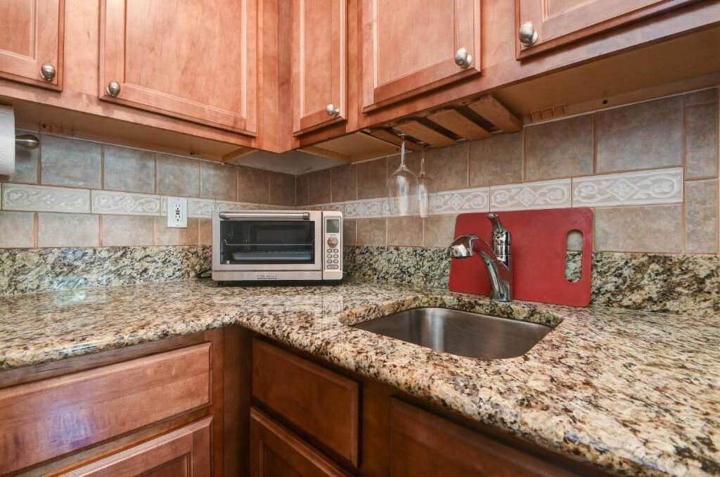 A kitchen with granite countertops, a built-in oven, a stainless steel sink, wooden cabinets, and a backsplash with patterned tiles.
