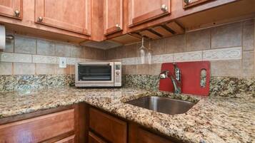 A kitchen with granite countertops, a built-in oven, a stainless steel sink, wooden cabinets, and a backsplash with patterned tiles.