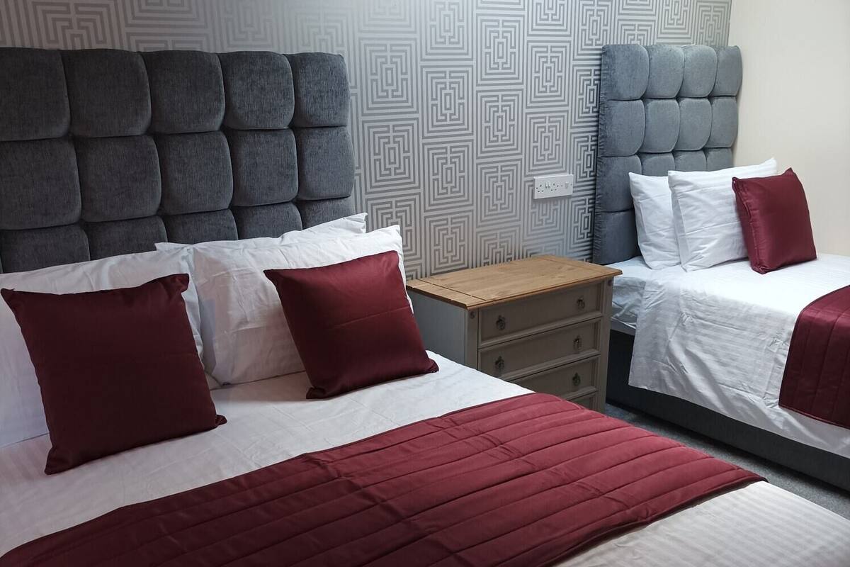 A hotel room with two beds, grey headboards, a wooden nightstand, and a patterned wall.