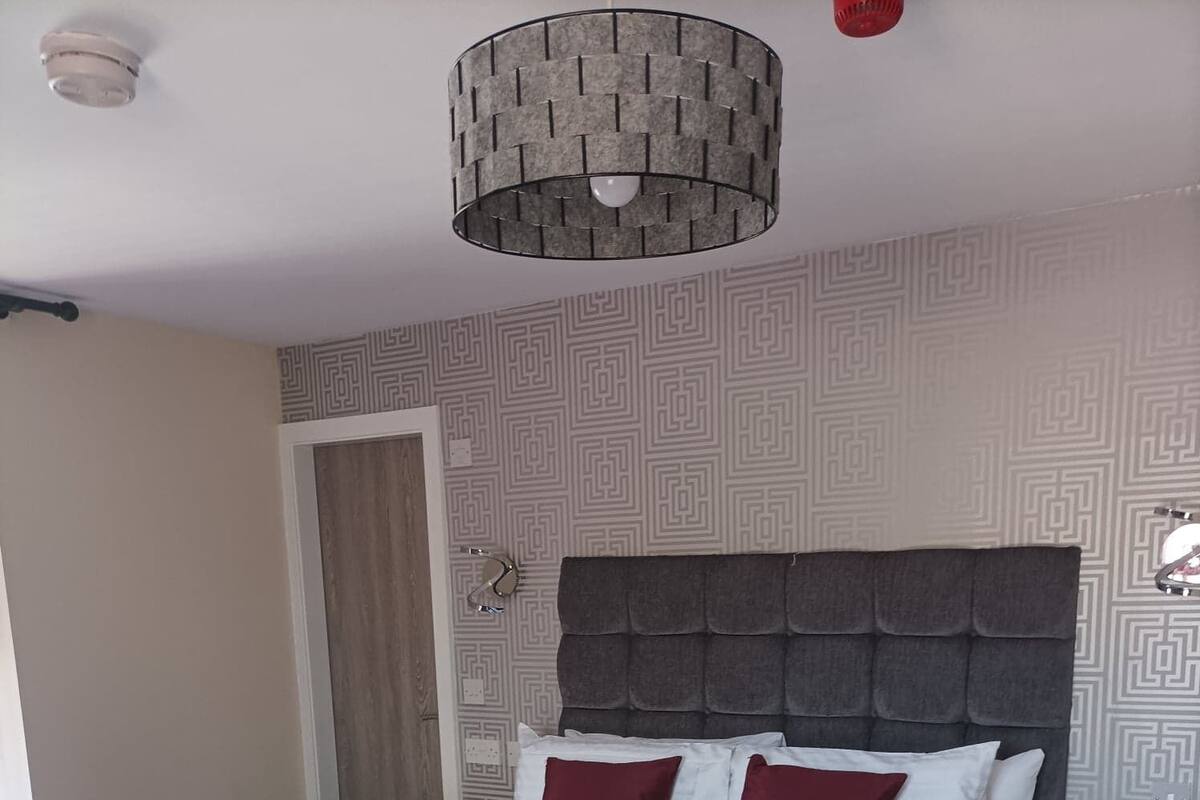 A neatly made bed with white and maroon bedding, a grey headboard, and a grey patterned wall.