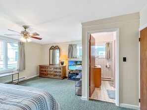 Ein Schlafzimmer mit Bett, Kommode, Deckenventilator, Fernseher und Blick auf einen Pool durch das Fenster.