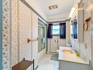 Ein Badezimmer mit floralem Wandpapier, einem Waschbecken inklusive Spiegel und einer Duschkabine.