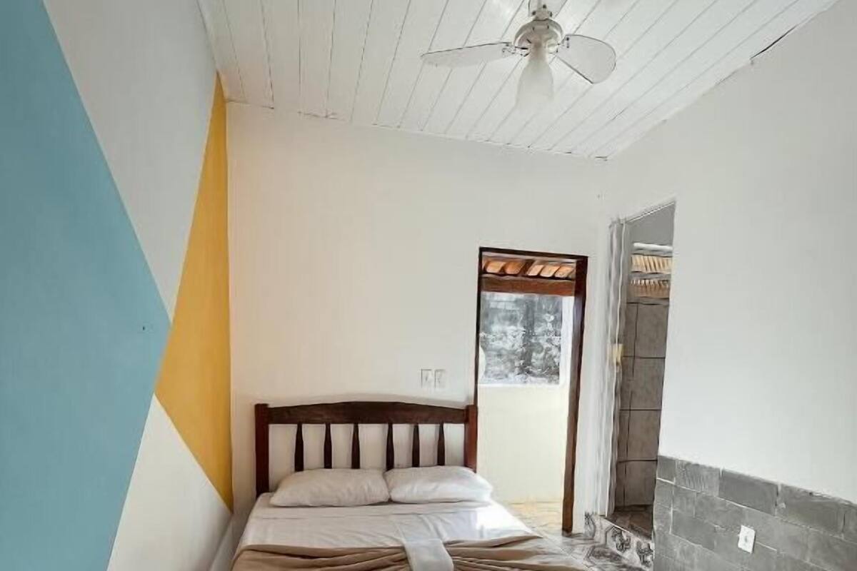 Ein Schlafzimmer mit einem Bett, einem Deckenventilator, einem Fenster und einer Tür zu einem Badezimmer.