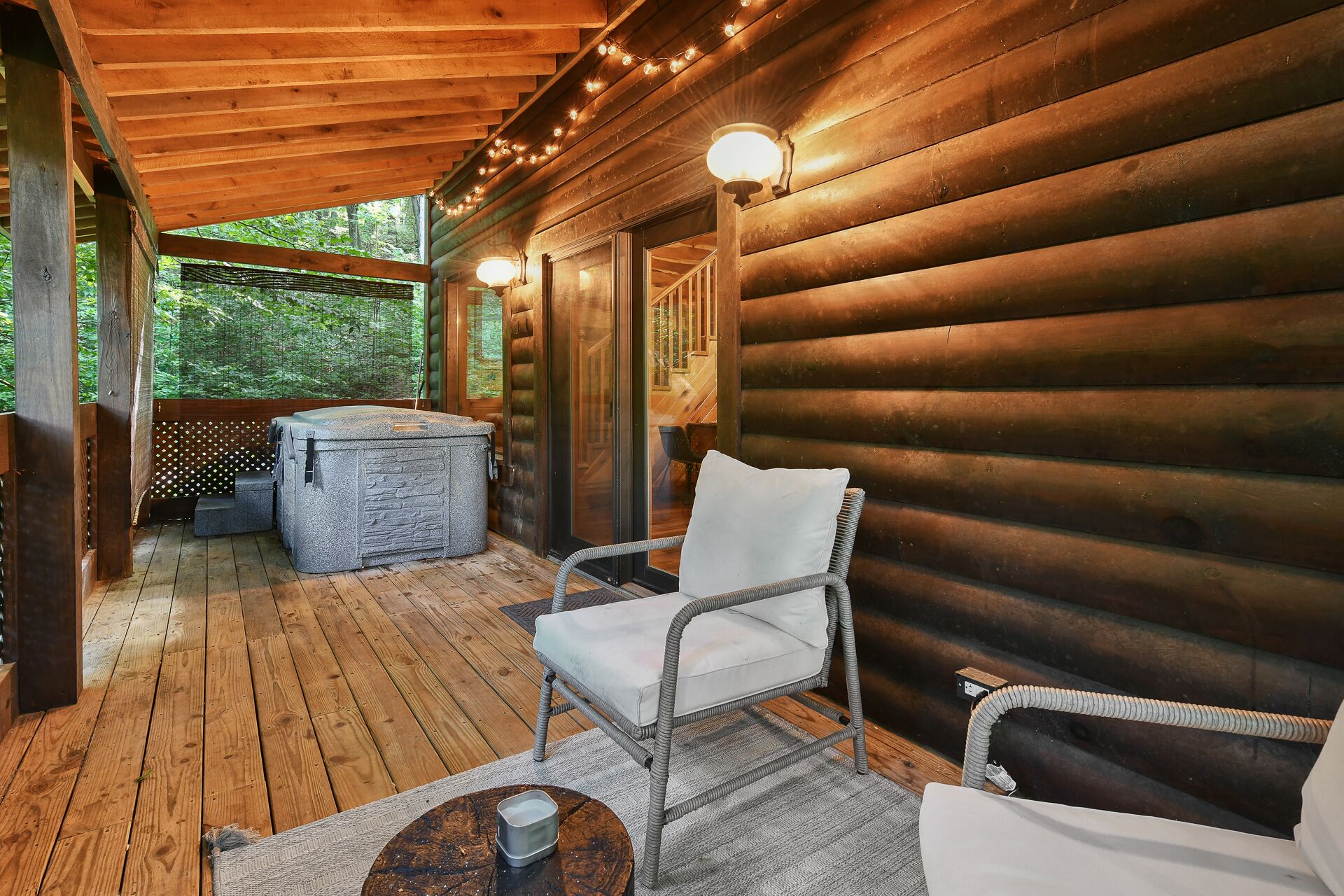 A wooden cabin with a covered porch, a hot tub, and a wicker chair.
