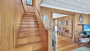 Een houten trap leidt naar een kamer met een televisie, schommelstoelen en een eethoek.