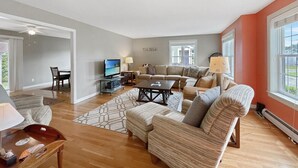 Uma sala de estar com sofá seccional, televisão e um espaço de jantar com mesa e cadeiras.