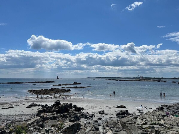 Ein felsiger Strand mit blauem Himmel und einem Leuchtturm in der Ferne.