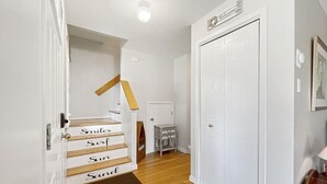 Uma escadaria com degraus marcados com as palavras 'Sorrisos', 'Surf', 'Sol' e 'Areia', conduzindo a uma porta com uma placa de 'Bem-vindo' em cima.