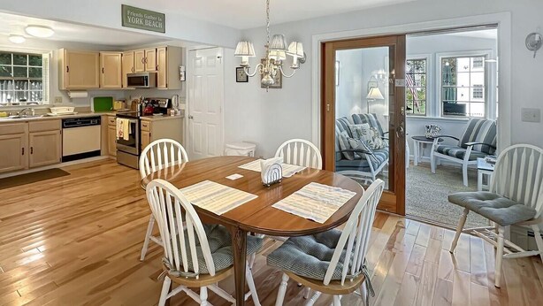 A dining area with a wooden table and white chairs, a kitchen with light-colored cabinets, and a view through a glass door to a seating area. - Family Retreat at York Beach (York Beach)