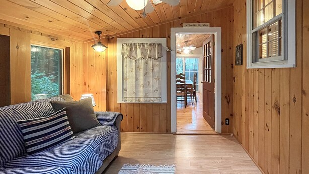 A cozy cabin interior with a wooden floor, a striped sofa, a ceiling fan, and a dining area visible through an open door. - Dewey Cottage (York Beach)