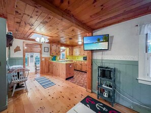 Ein Holzhütten-Interieur mit Küche, Essbereich und einem an der Wand befestigten Fernseher.