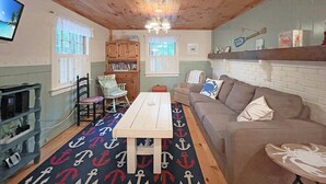 A cozy room with a wooden ceiling, a wooden table, a sofa, and a bookshelf. - Dewey Cottage (York Beach)