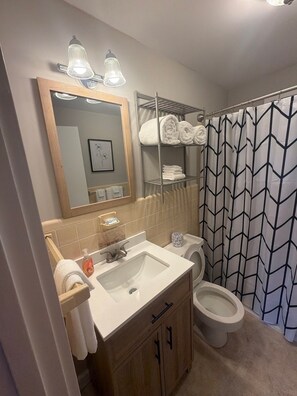 A bathroom with a sink, mirror, towel rack, toilet, and shower curtain.