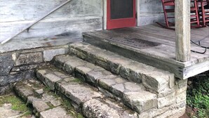 A rustic wooden house with a porch, a red door, and a stone staircase leading to the entrance.