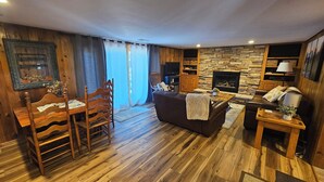 Un accogliente soggiorno con camino in pietra, pavimento in legno, un divano in pelle e un'area pranzo con tavolo e sedie in legno.