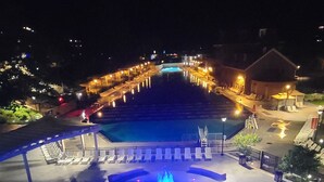 Vista notturna di una zona piscina con fontana centrale, circondata da lettini e un'area salotto coperta.