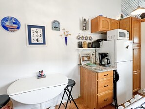 A compact kitchen with a white table, wooden cabinets, a microwave, and a coffee maker. - Lighthouse - Q991 (Cape Neddick)