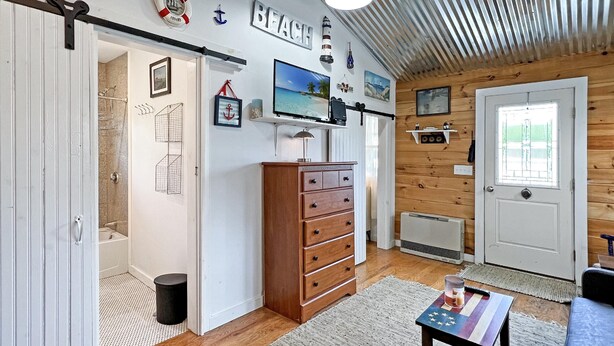 A room with a wooden ceiling, a television mounted on the wall, a wooden dresser, and a door with a window. - Lighthouse - Q991 (Cape Neddick)