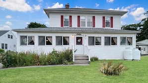 A two-story white house with red shutters, a front porch, and a small garden. - Kurtz Cottage (York Beach)