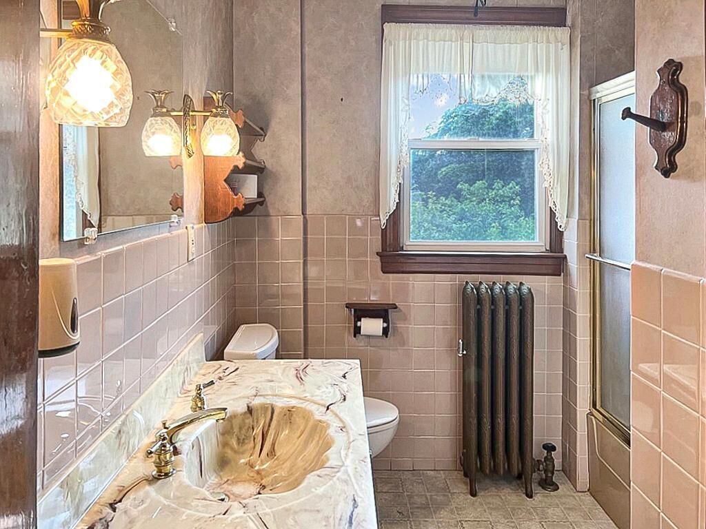 Ein Badezimmer mit Marmorwaschbecken, Toilette, Fenster mit Blick auf Grünflächen und einer Heizung.