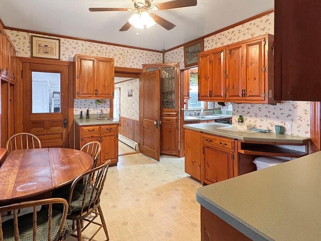 A kitchen with wooden cabinets, a dining table with chairs, and a ceiling fan.
