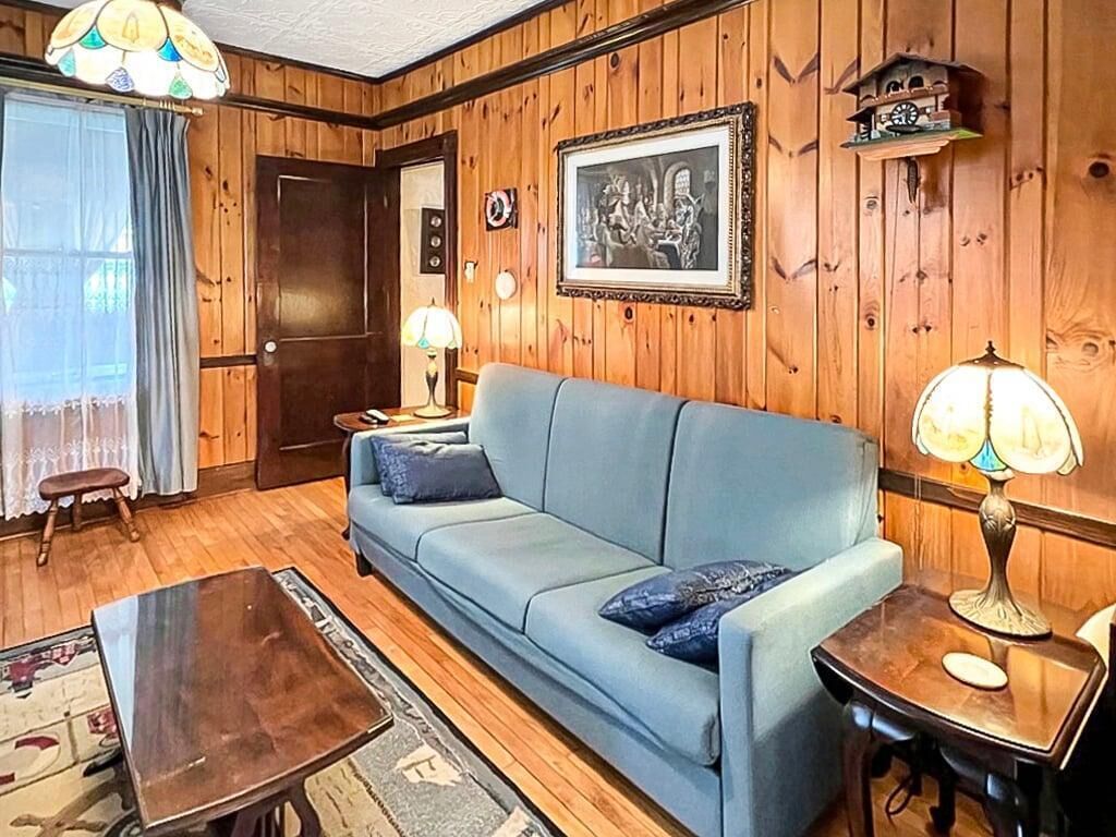 A room with a wooden paneled wall, a blue sofa, a wooden coffee table, a lamp, and a framed picture on the wall.