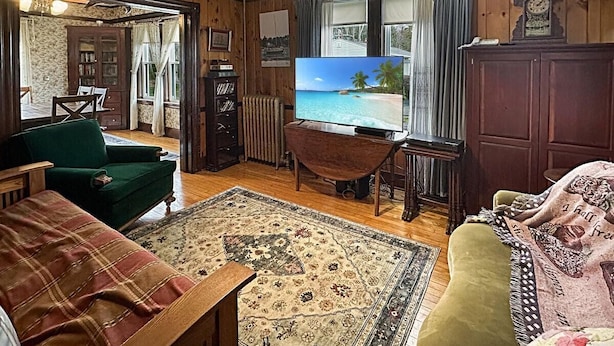 A cozy living room with a television, wooden walls, a green armchair, a patterned rug, and a wooden cabinet. - Kurtz Cottage (York Beach)