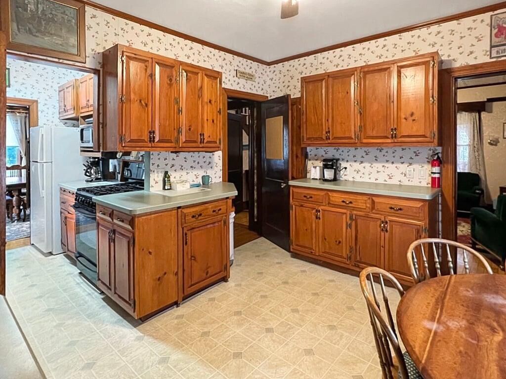 A kitchen with wooden cabinets, a stove, a refrigerator, and a dining table with chairs.