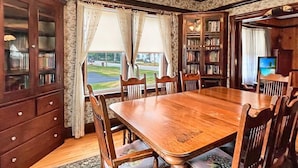 A dining room with a wooden table and chairs, a bookshelf, and a view of the outdoors. - Kurtz Cottage (York Beach)