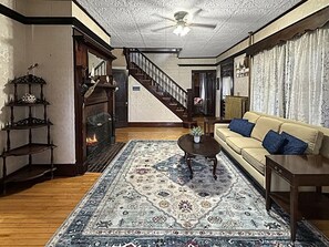 Ein Wohnzimmer mit Holzboden, einer Couch, einem Couchtisch, einem Kamin, einer Treppe und einem Deckenventilator.